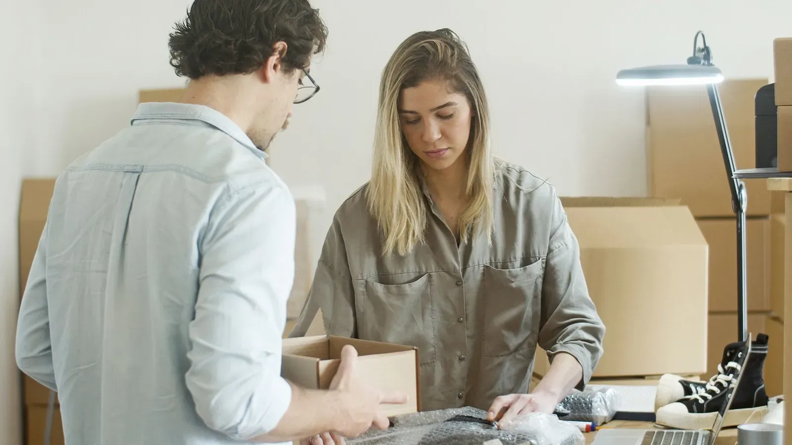 Zwei junge Erwachsene packen Bekleidungsartikel in einem Büro für ihr Online-Shop-Startup.