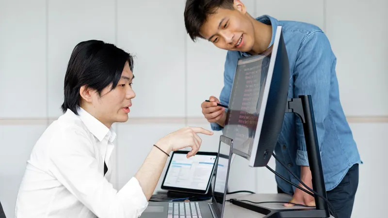 Zwei asiatische Männer arbeiten in einem Büro zusammen an einem Projekt mit Computern.
