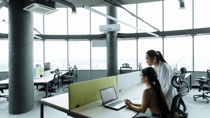 Zwei asiatische Frauen, die in einer modernen Büroumgebung zusammenarbeiten, die sich auf Teamarbeit und Innovation konzentriert.