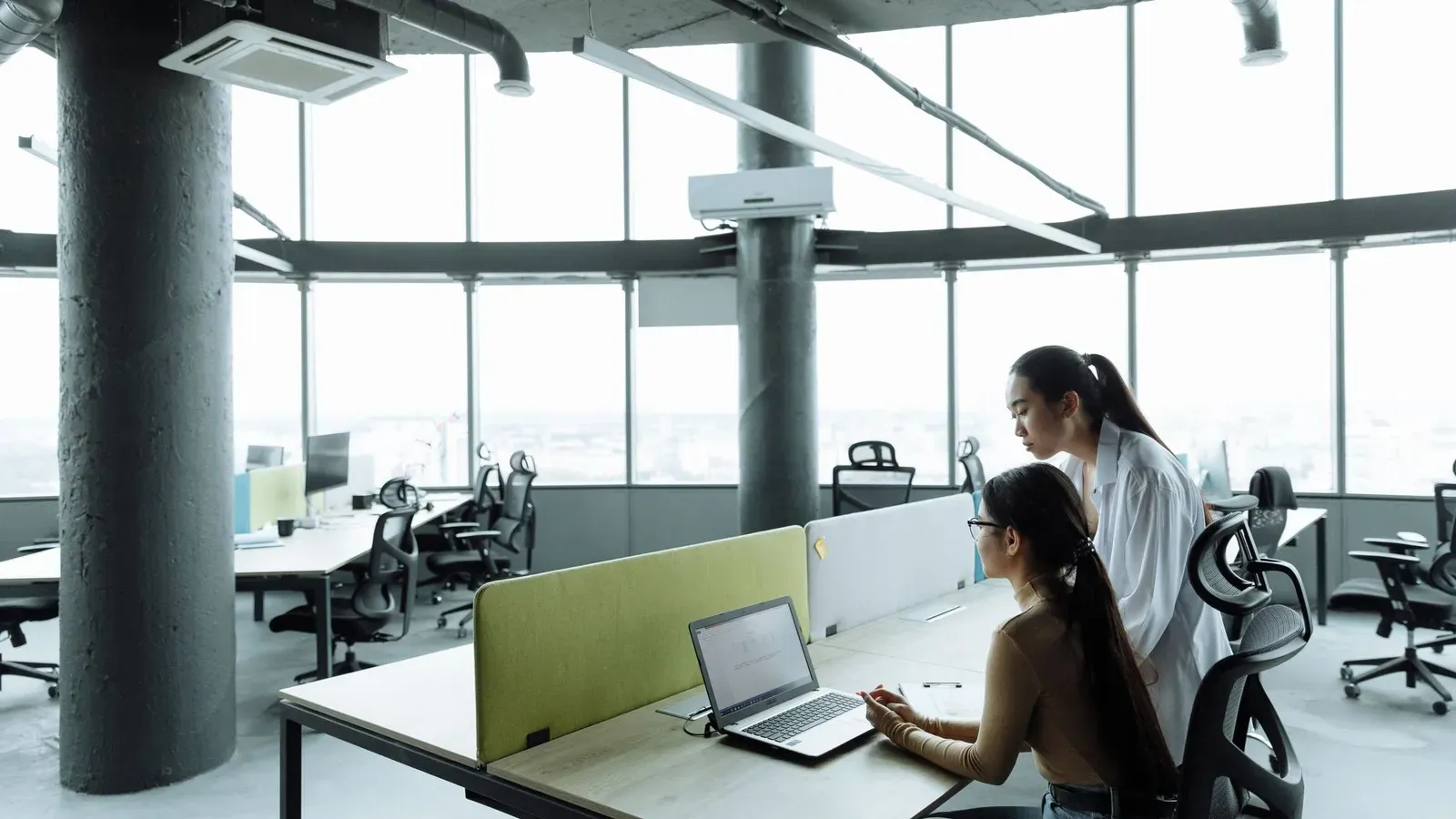 Zwei asiatische Frauen, die in einer modernen Büroumgebung zusammenarbeiten, die sich auf Teamarbeit und Innovation konzentriert.