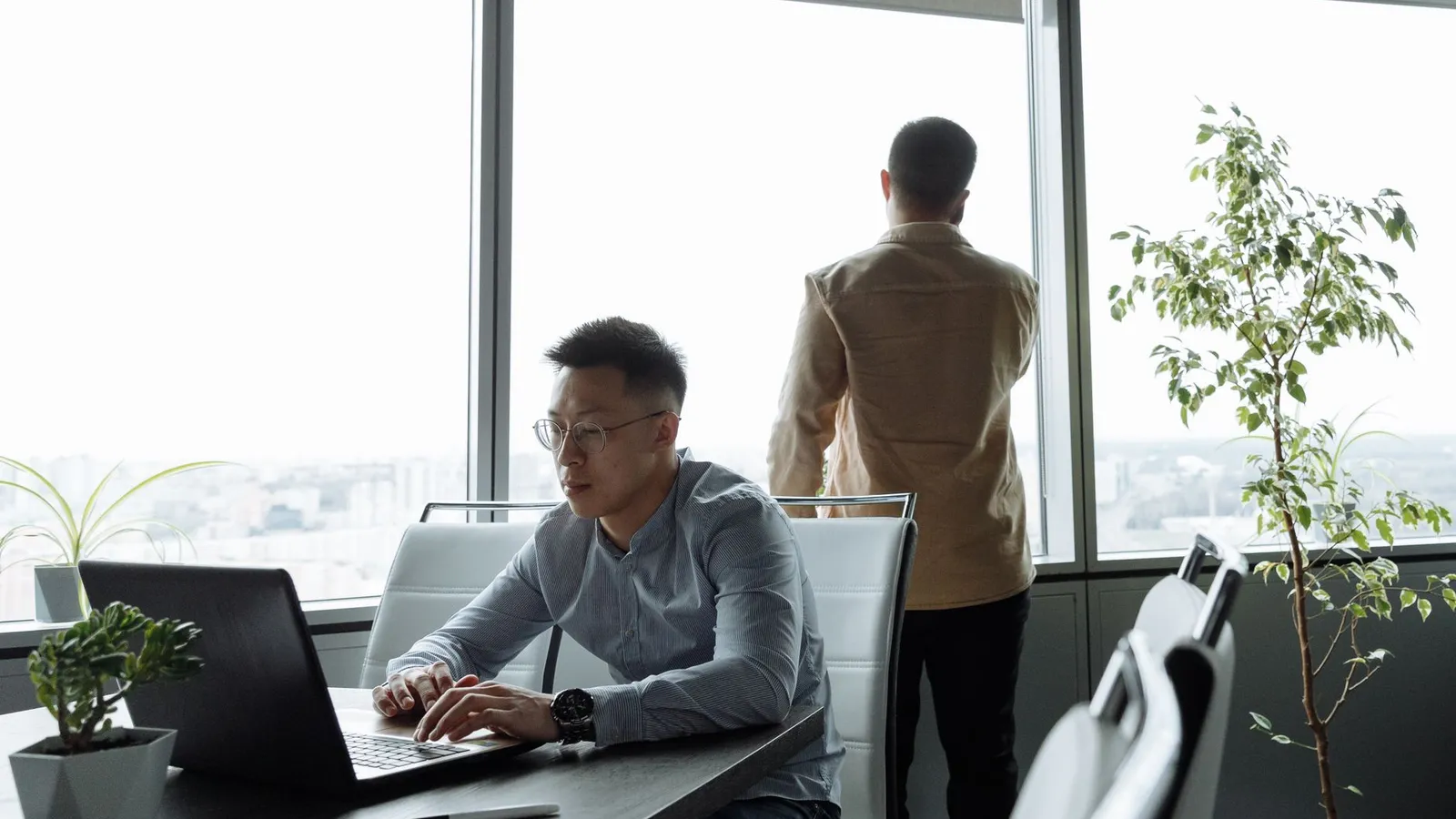 Zwei Männer arbeiten in einem modernen Büro mit großen Fenstern und Blick auf die Stadt.
